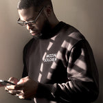 Man wearing a Moon Soldier black soft cotton crewneck sweatshirt, standing in soft lighting while holding a phone.