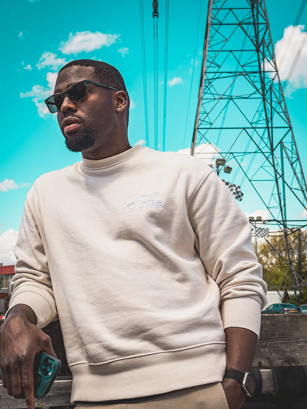 Man wearing a cream soft cotton heavy sweatshirt with the Moon Soldier logo embroidered on the chest, styled with sunglasses and a casual outdoor setting.