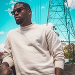 Man wearing a cream soft cotton heavy sweatshirt with the Moon Soldier logo embroidered on the chest, styled with sunglasses and a casual outdoor setting.