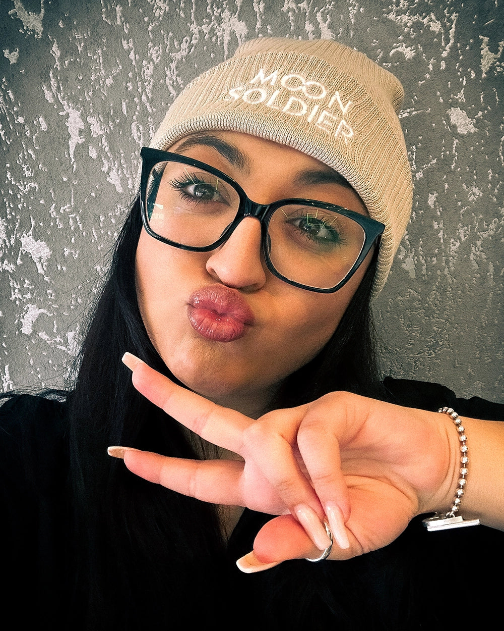 Model wearing a beige Moon Soldier soft cotton beanie, making a peace sign with a cozy and stylish vibe.